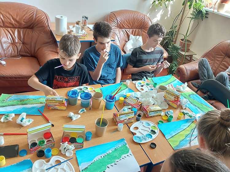 3 chłopców siedzi przy stole, coś maluje