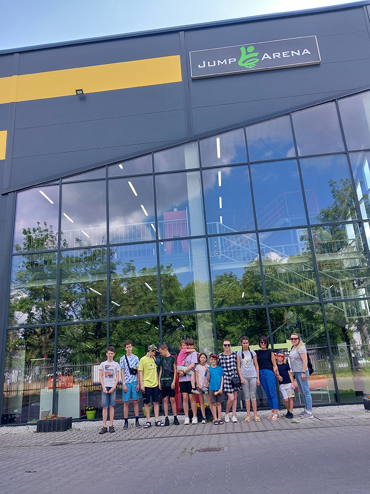 Grupa dzieci i dorosłych stoi przed przeszklonym budynkiem