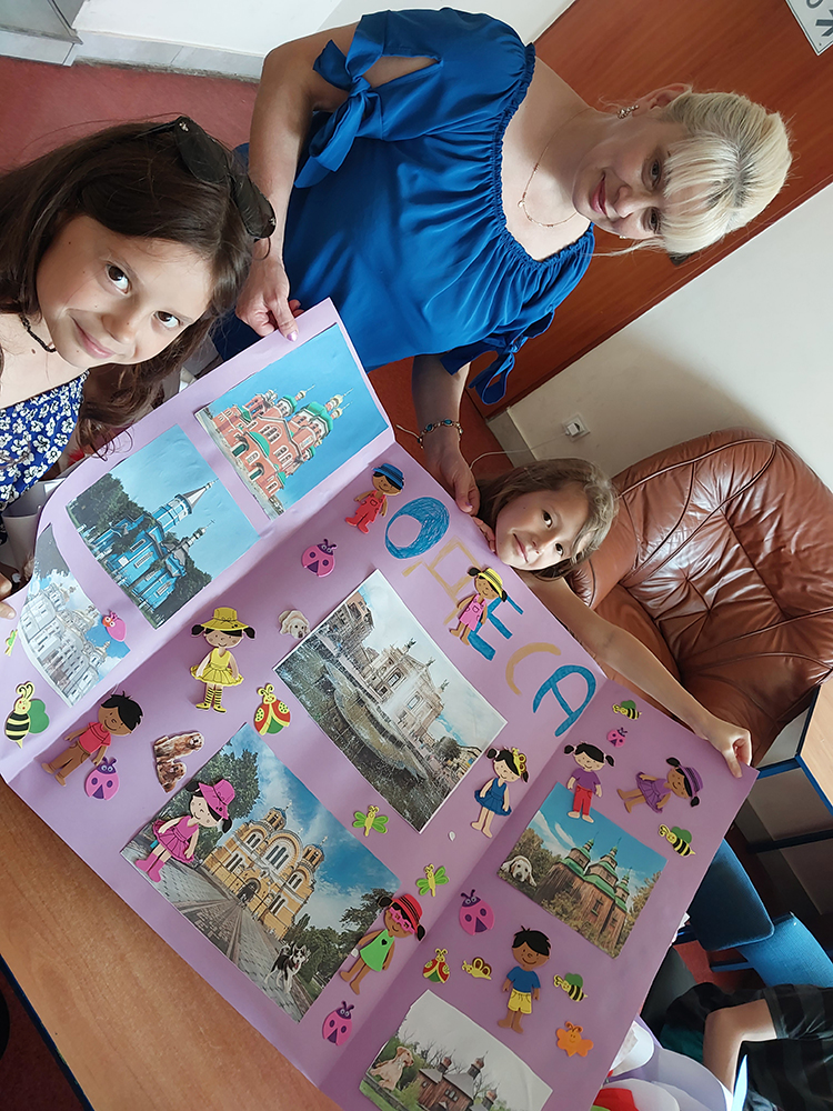 Kobieta i 2 dziewczynki pokazują naklejone na brystolu zdjęcia