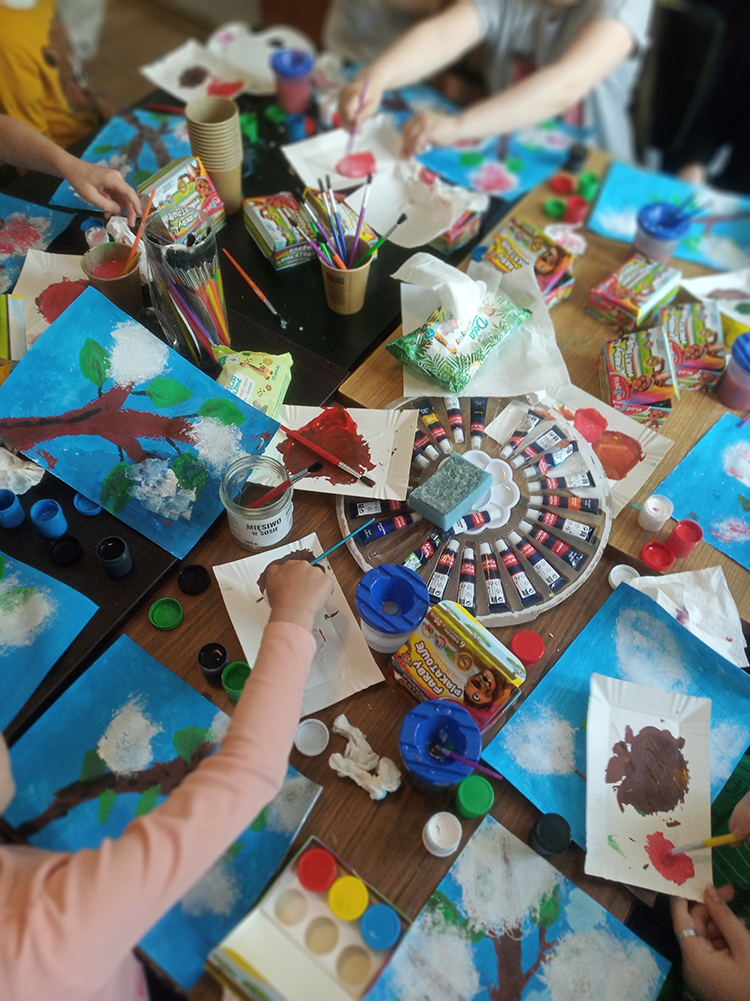 Na stole leża rysunki, farby i pędzle